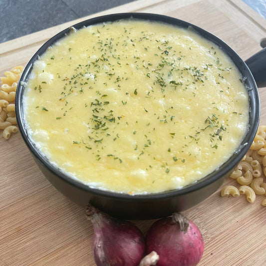 Macaroni and cheese in a black pot on a wooden surface with onions and pasta.