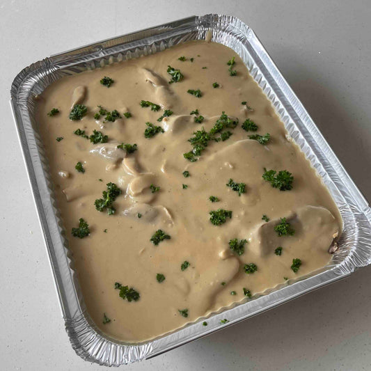 Aluminum pan with creamy dish topped with green herbs on a white surface